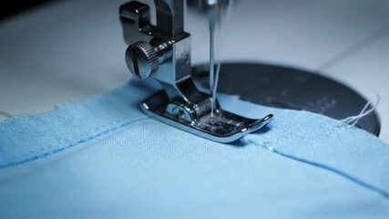 A sewing machine's presser foot and needle meticulously stitch a seam on light blue fabric.