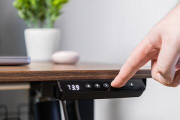 Hand adjusts ergonomic standing desk height using a sleek control panel displaying 73.9, promoting...