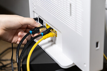 Adult hand firmly inserting a crucial black Ethernet LAN network cable into a modern white Wi-Fi router, enabling swift internet connectivity and robust digital network access