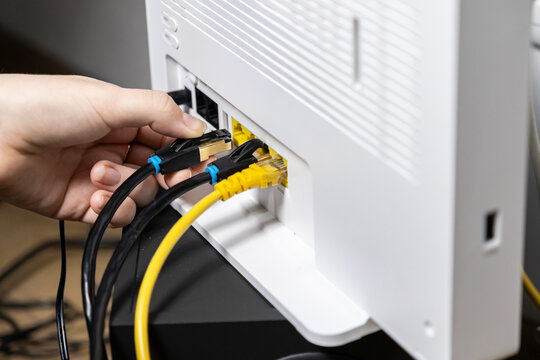 Adult hand firmly inserting a crucial black Ethernet LAN network cable into a modern white Wi-Fi router, enabling swift internet connectivity and robust digital network access