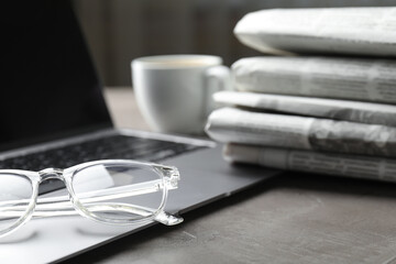 Newspapers, laptop and glasses on grey table, closeup
