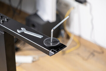 Allen key is meticulously adjusting a modern desk leg leveler, accompanied by a small wrench, signifying precise furniture assembly and practical home improvement
