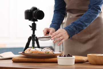 Woman creating composition with croissants at table in studio, closeup. Professional food photography