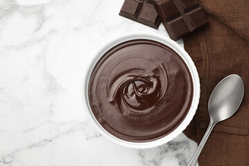 Melted chocolate in bowl, pieces and spoon on white marble table, flat lay. Space for text