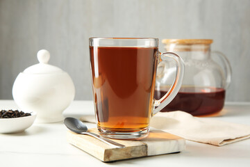 Tasty tea in glass cup and teaspoon on white table against grey background, closeup