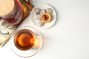 Tasty tea in glass cup, teapot and Turkish desserts on white table, flat lay. Space for text