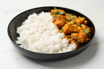 Chicken tikka masala with rice and parsley in bowl on white marble table, closeup