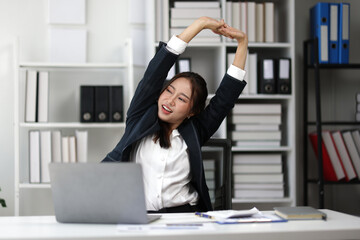 Asian businesswoman relaxing at her office desk, stretching her arms after working. Taking a...