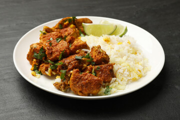 Delicious chicken tikka masala with rice, parsley and lime on dark textured table, closeup