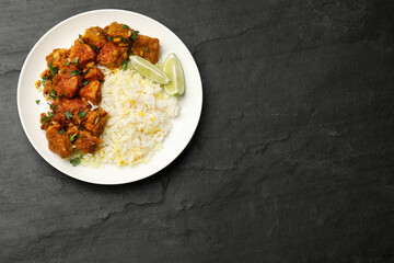 Delicious chicken tikka masala with rice, parsley and lime on dark textured table, top view. Space for text