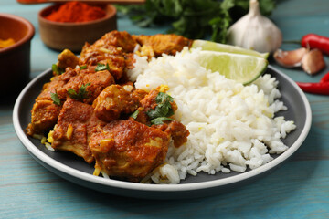 Delicious chicken tikka masala with rice, parsley, lime and spices on light blue wooden table, closeup