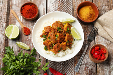 Delicious chicken tikka masala with rice, parsley, lime and spices served on color wooden table, flat lay
