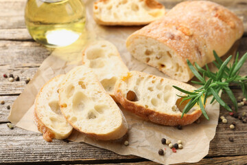 Ciabatta slices, oil, peppercorns and rosemary on wooden table, closeup