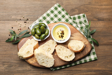 Fototapeta premium Ciabatta slices, oil with peppercorns and olives on wooden table, flat lay