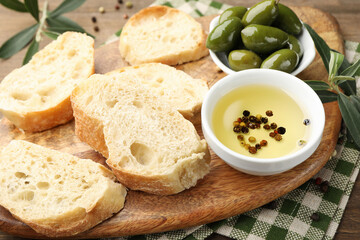 Ciabatta slices, oil with peppercorns and olives on wooden table, closeup