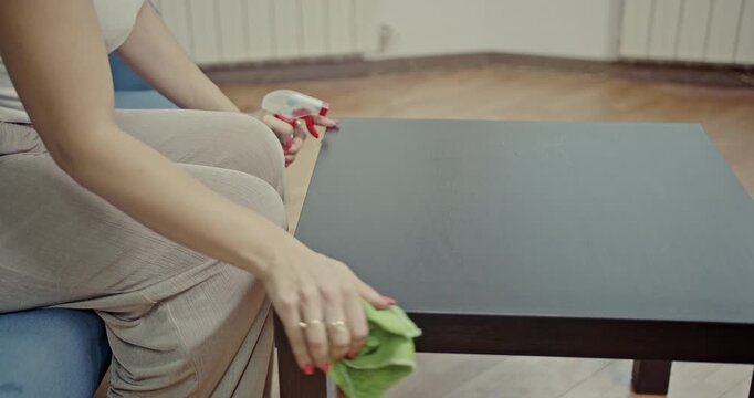 Experience the satisfying sounds of daily chores as a woman meticulously cleans a wooden table with a spray bottle and cloth, ensuring a pristine and tidy home environment.