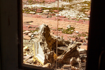 A poignant view through a dilapidated doorway reveals a crumbled facade, its remnants strewn amidst scattered tiles and verdant moss, symbolizing forgotten histories and nature's slow reclaim