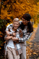 Fototapeta premium A mother and her son are walking in the fall, having fun together. A family walk through the yellow leaves in the fall