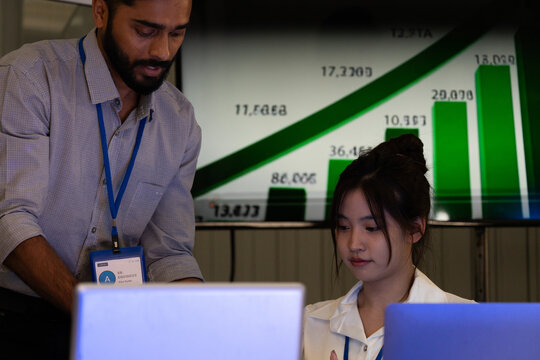 Business team analyzing data on laptops with growth chart in background. Diverse professionals collaborating in office, discussing financial performance, strategy, and success analytics in workplace.