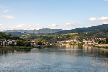 Fototapeta premium A small coastal town with houses and buildings, located by a calm river, surrounded by wooded hills