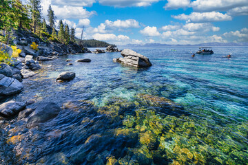 Kayakers and boat near Bonsai Rock at Lake Tahoe Nevada USA on sunny summer day with clear turquoise wate, granite boulders, pine trees and blue sky with white clouds in scenic Sierra Nevada landscape
