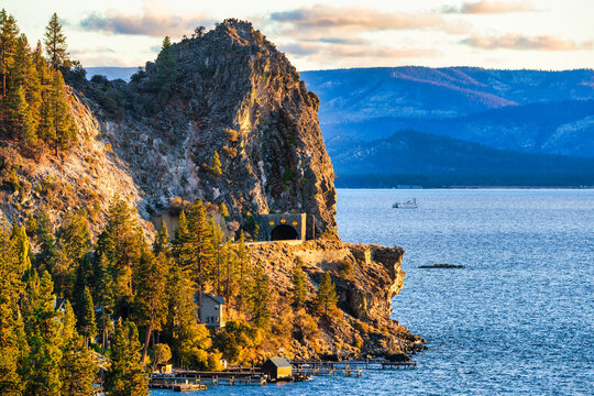 Cave Rock Tunnel on east shore of Lake Tahoe Nevada USA at golden sunset with boat on blue water and pine forest along rocky mountain cliffs in Sierra Nevada scenic landscape travel destination