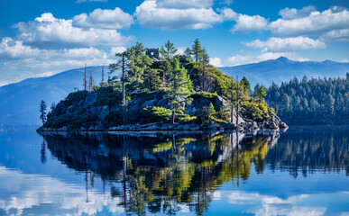 Fannette Island in Emerald Bay State Park at Lake Tahoe California USA with stone tea house ruins surrounded by pine trees reflected in calm blue water and Sierra Nevada mountains on sunny summer day