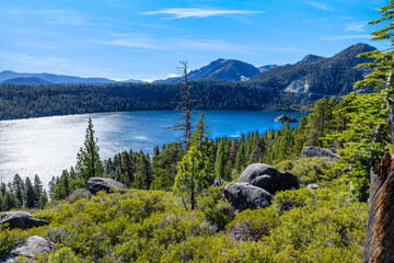 Sunny panoramic view of Emerald Bay and Fannette Island at Lake Tahoe California USA with clear blue water surrounded by pine forest mountains and granite rocks under bright summer sky