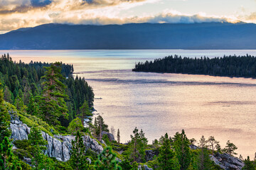 Panoramic view of Emerald Bay and Lake Tahoe California USA at sunset with calm water reflecting warm light surrounded by pine forest mountains and dramatic clouds above Sierra Nevada landscape