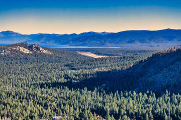Lake Tahoe, California USA panoramic mountain landscape with blue lake water, evergreen pine forest, and distant Sierra Nevada peaks under clear sky, scenic natural view and outdoor travel destination