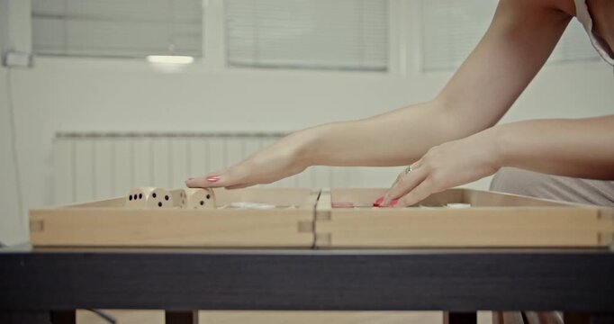 Watch a detailed close-up of a woman's hands skillfully rolling dice and strategically moving checkers on a backgammon board, complete with immersive game sounds. Perfect for illustrating leisure.