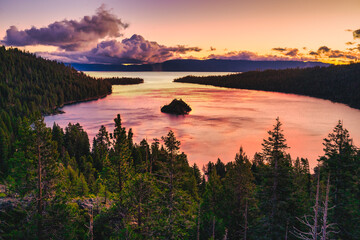 Emerald Bay State Park at Lake Tahoe California USA sunrise view with Fannette Island reflecting calm pink water surrounded by pine forest mountains and dramatic colorful sky scenic nature landscape
