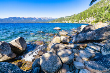 Lake Tahoe California USA view of clear turquoise water with granite rocks and pine forest along mountain shore under blue sky with clouds scenic summer landscape of Sierra Nevada nature