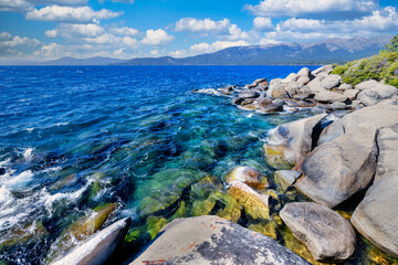 Lake Tahoe California USA view of clear turquoise water with granite rocks and pine forest along mountain shore under blue sky with clouds scenic summer landscape of Sierra Nevada nature