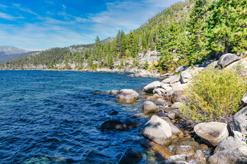 Lake Tahoe California USA view of clear turquoise water with granite rocks and pine forest along mountain shore under blue sky with clouds scenic summer landscape of Sierra Nevada nature