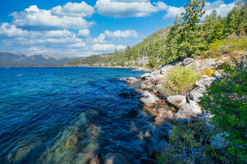 Lake Tahoe California USA view of clear turquoise water with granite rocks and pine forest along mountain shore under blue sky with clouds scenic summer landscape of Sierra Nevada nature
