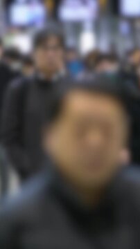Defocused vertical capture of Asian commuters walking across intersection in Tokyo, suggesting modern routine, societal rhythm, and anonymity in urban environments.