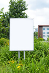 Blank billboard in a lush green outdoor setting with a modern building in the background.