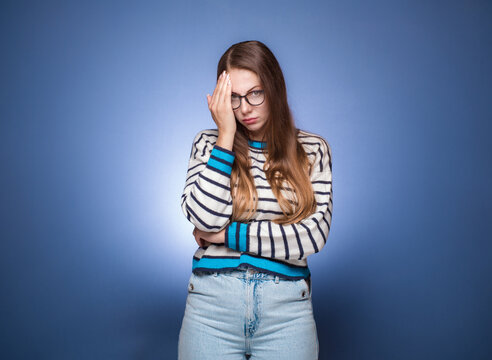 Ashamed woman covering face with hand. Shame, isolated on blue background. Guilty girl.