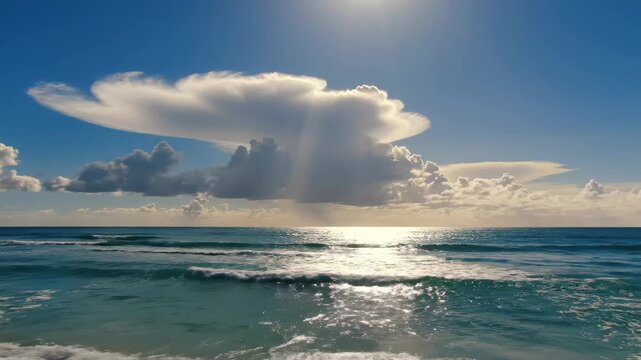 Sunlit ocean view with dramatic clouds - This video showcases a bright, sunny day at the ocean, highlighting a large, striking cumulonimbus cloud formation dominating the sky above the sparkling sea.