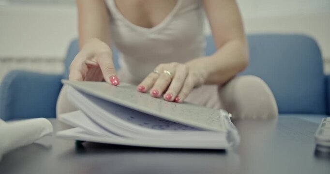 Witness a young woman creating satisfying ASMR sounds using a spiral-bound notebook and a metal pencil case at home. Her focused actions highlight the therapeutic and calming audio experience.