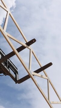 Construction workers operate telehandler crane to raise large wooden beams at building site under frame assembly