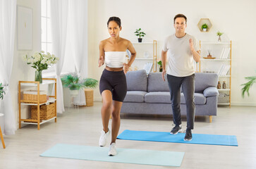 Couple family workout at home together. They perform cardio exercise on soft mats in a bright...