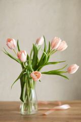 A bouquet of delicate pink tulips in a glass vase on a wooden table.