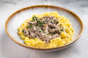 Plate of tender beef stroganoff served with creamy mashed potatoes and steaming gravy. grey background. top view