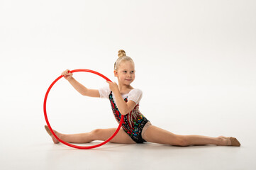 Girl gymnast with cochlear implant performing split with red hoop. Combination of hearing technology, discipline, and inclusion in rhythmic gymnastics and childhood art. © satura_