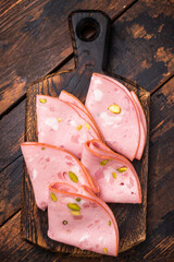 Italian Mortadella sausage slices with pistachios on wooden cutting board. wooden background. top view © Mironov