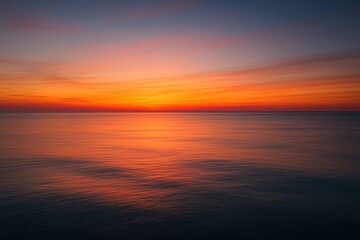 Fototapeta premium As the sun sets, the sky displays shades of orange, pink, and purple while calm waters reflect these colors, making a peaceful scene near the coastline during twilight