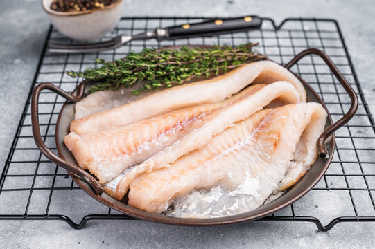 Raw Hake fish fillet in steel tray with herbs. grey background. top view