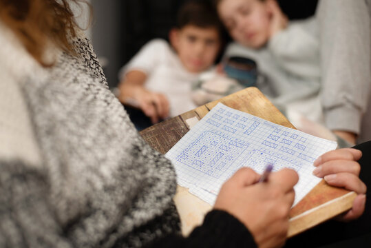 A woman as a good mother spends time with her children, they play the board game Sea Battle together, draw on pieces of paper, laugh, have good time together